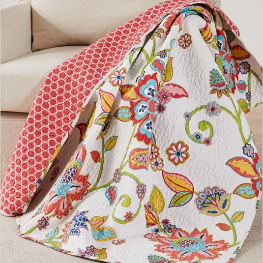 A colorful quilt with vibrant floral designs is draped over a beige couch. The reverse side features a red geometric pattern.