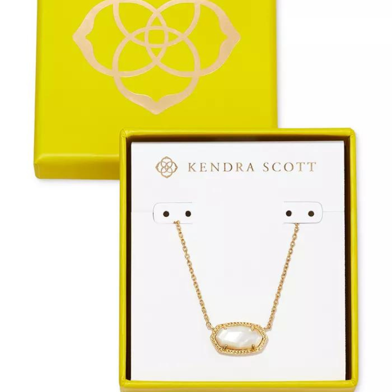 A gold-colored Kendra Scott necklace with an elongated, faceted stone pendant and a delicate chain is displayed in a bright yellow box with the brand logo.