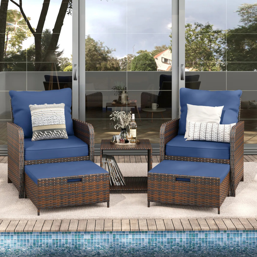 Outdoor seating set with two wicker armchairs, blue cushions, matching ottomans, and a side table, all positioned by a pool.