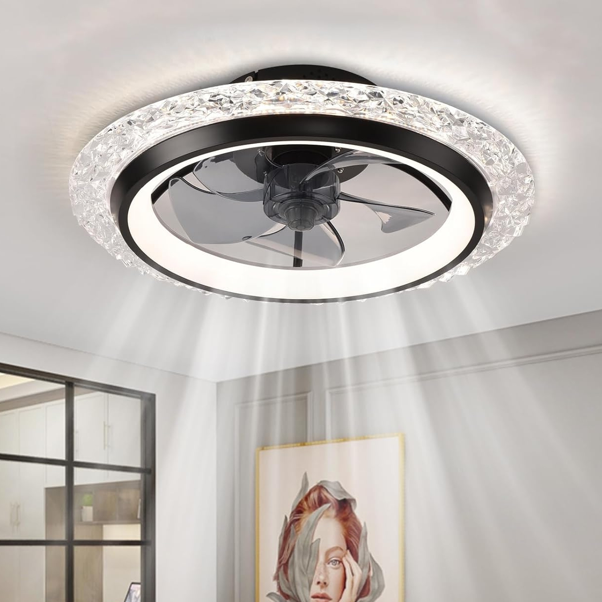 A modern ceiling fan with integrated lights features a circular design with a crystal-like border and a sleek black center housing the fan blades. The lighting emits a soft glow, creating a stylish and functional fixture for the room.