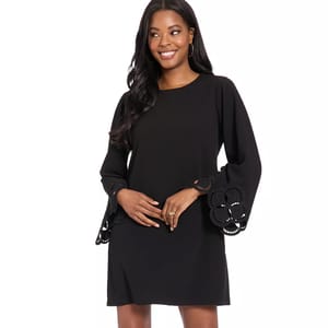 A woman wearing a black long-sleeve dress with flared cuffs featuring intricate cutout designs, complemented by gold hoop earrings.