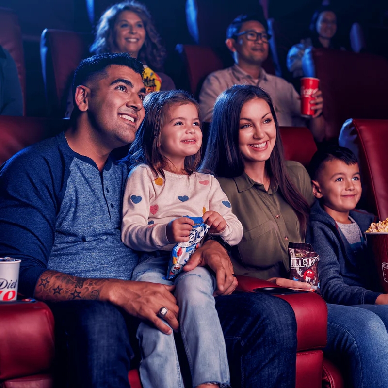 A family is enjoying snacks and drinks while seated in a movie theater. They have popcorn, M&M's, and a soft drink.