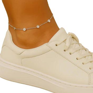 A cream-colored sneaker with a simple design is worn with a delicate silver anklet featuring small beads.