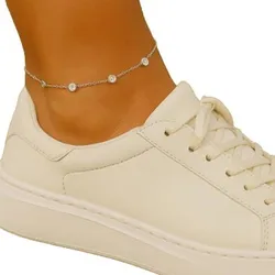A cream-colored sneaker with a simple design is worn with a delicate silver anklet featuring small beads.