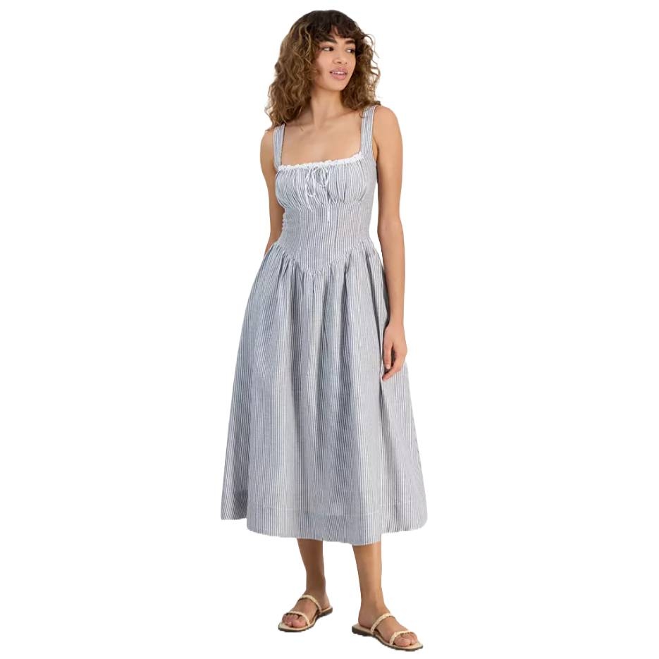 A woman is wearing a sleeveless, blue and white striped midi dress with a gathered bodice and a flowing skirt, paired with flat sandals.