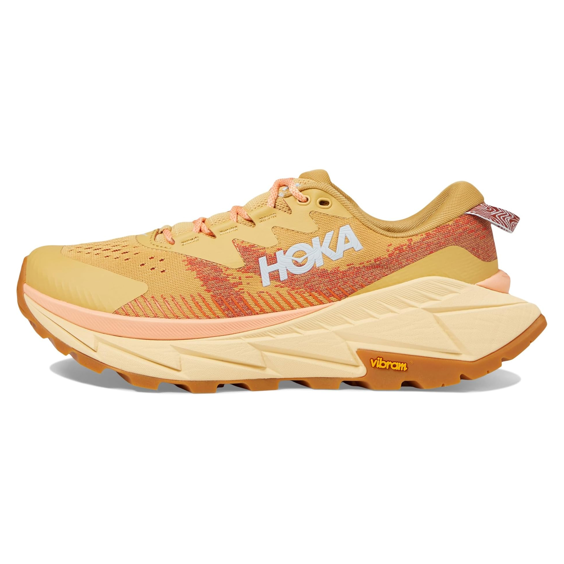 Hoka Skyline Float X shoes feature a golden-yellow color with orange and coral accents, a thick cushioned sole, and a Vibram outsole for enhanced grip. Designed for comfort and performance, they have the Hoka logo prominently displayed on the side.