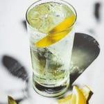 A glass of clear carbonated beverage with ice cubes and lemon slices.