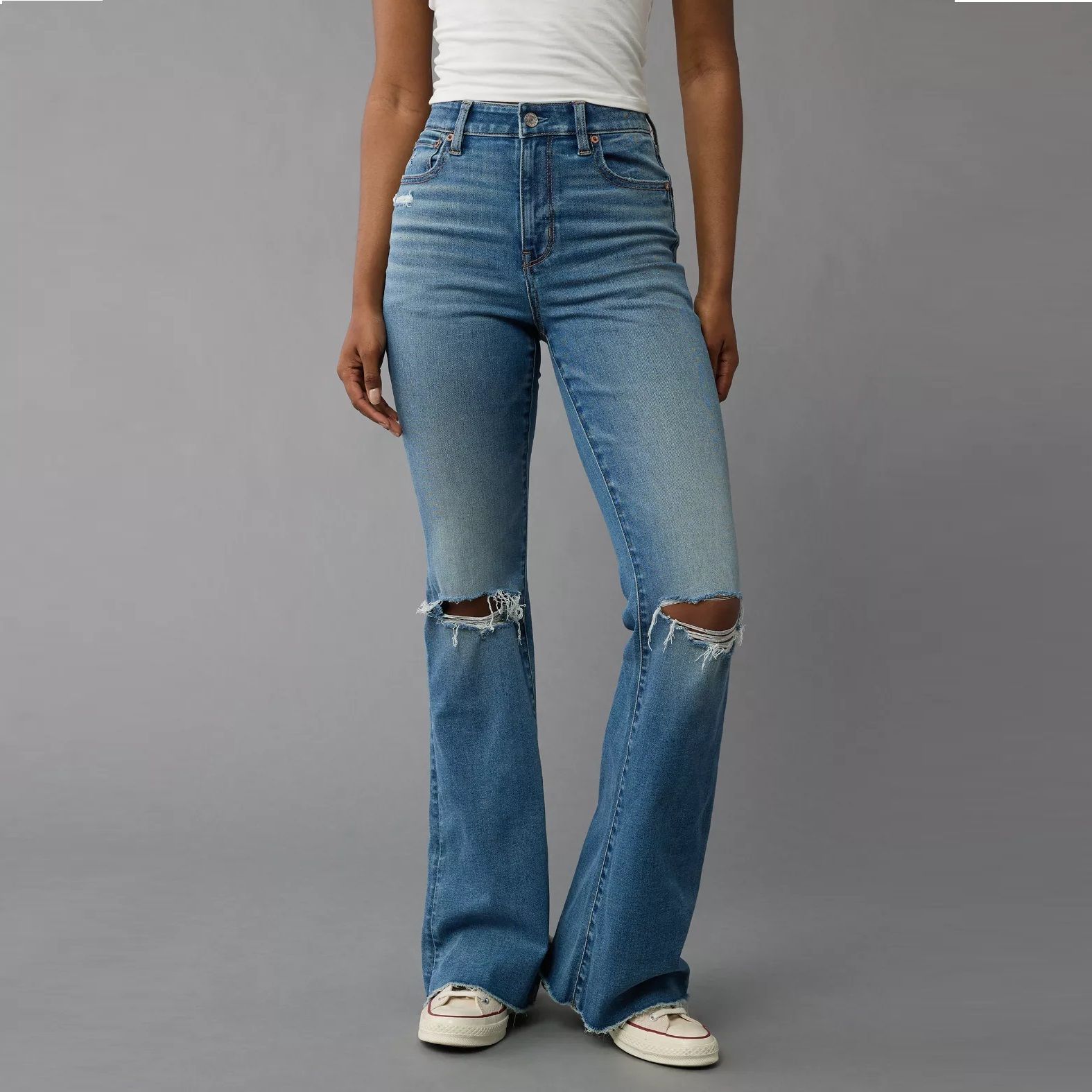 A person wearing ripped blue flared jeans with white sneakers.