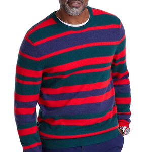 A man is wearing a colorful striped sweater with red, green, and dark purple horizontal stripes, paired with a watch and dark trousers.