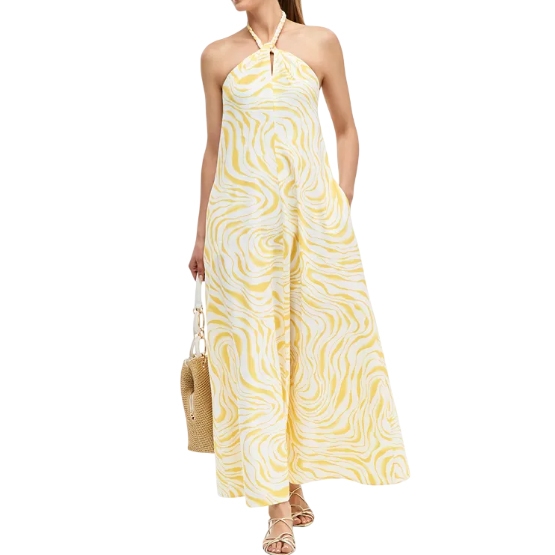 A woman is wearing a halter-neck yellow and white patterned maxi dress, holding a woven handbag. She is also wearing sandals.