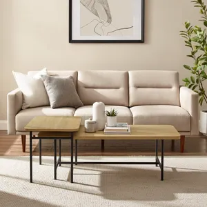 A beige sofa with a tufted design is accompanied by a dual-level wooden coffee table with metal legs, set on a textured rug. A minimalist abstract art piece is framed above, and a tall potted plant adds greenery to the room.