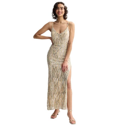 A model wearing a sparkling gold evening gown with thin straps, intricate sequin detailing, and a high leg slit, paired with matching gold heels.