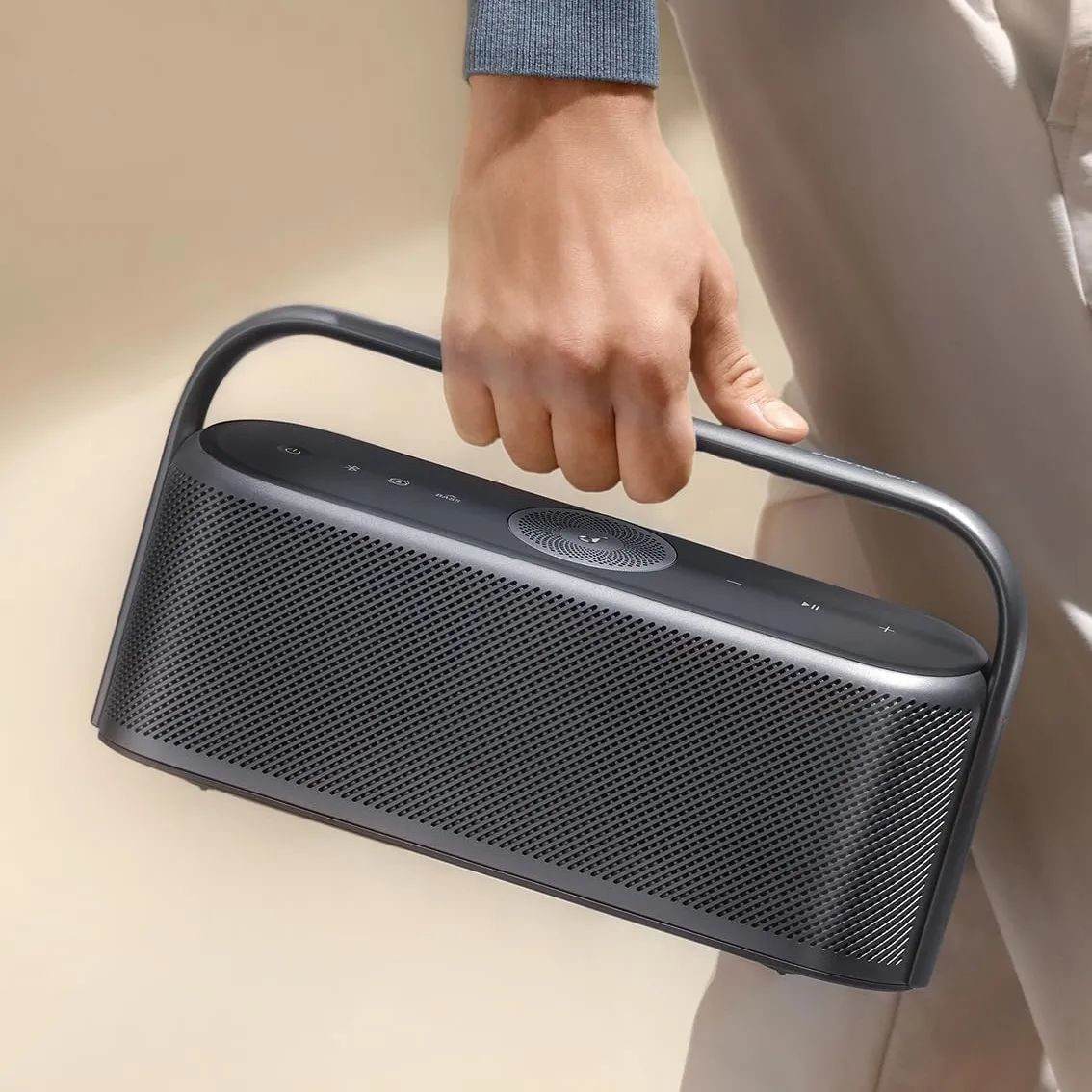A person is holding a portable Bluetooth speaker with a carrying handle.