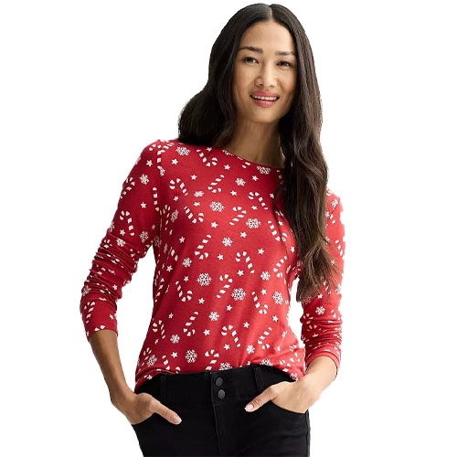 A woman wearing a red, long-sleeve shirt with a white snowflake and floral pattern, paired with black pants.
