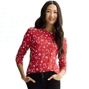 A woman wearing a red, long-sleeve shirt with a white snowflake and floral pattern, paired with black pants.
