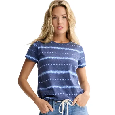 A woman wears a short-sleeve navy blue T-shirt with white horizontal tie-dye stripes, paired with light blue jeans featuring a white drawstring.
