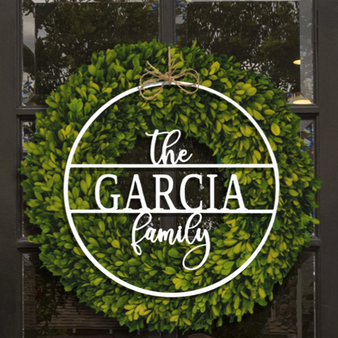 A decorative green wreath with a white overlay displays the text \“The Garcia Family,\“ hanging on a glass-paneled door, tied with twine at the top.