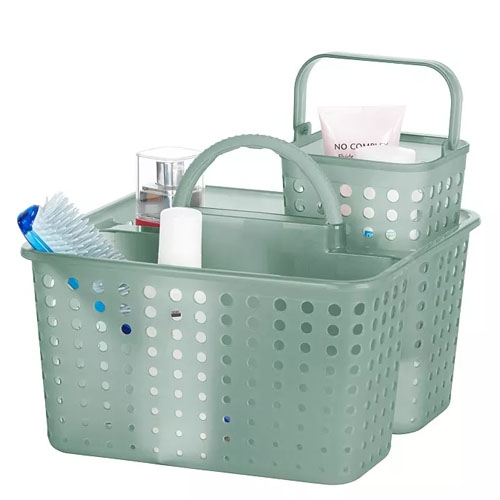 Two green plastic storage caddies with perforations, featuring handles and containing various bath and grooming items like a toothbrush, a tube, and a bottle.