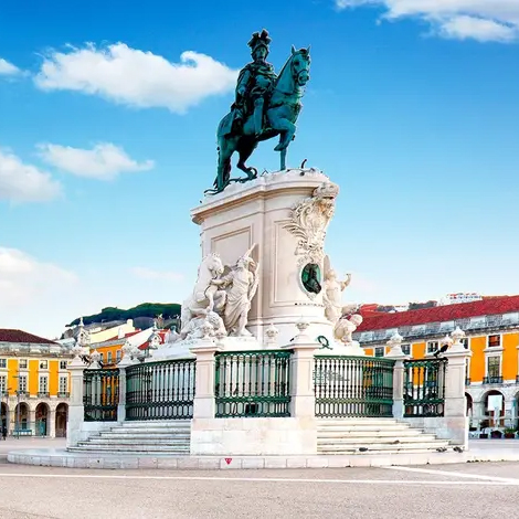 A statue depicting a rider on horseback is prominently displayed, surrounded by elaborate sculptures. The structure is set in a plaza with colorful historic buildings in the background.