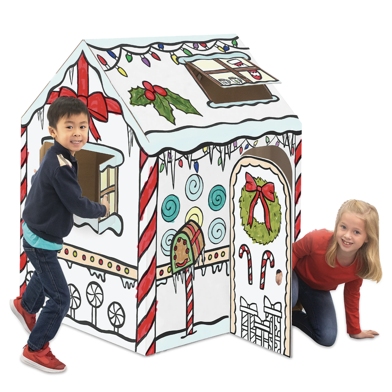 A cardboard playhouse designed like a gingerbread house, featuring holiday decorations such as candy canes, wreaths, and lights. Two children are interacting with the playhouse.