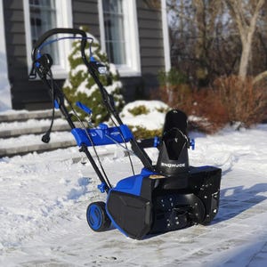A blue and black snowblower on a snowy driveway with a house in the background.