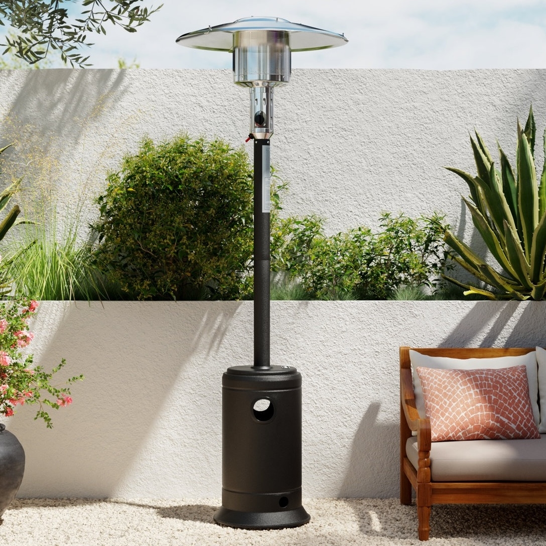 Outdoor patio heater with a black base and silver top, surrounded by a garden and a wicker chair with a pink cushion.