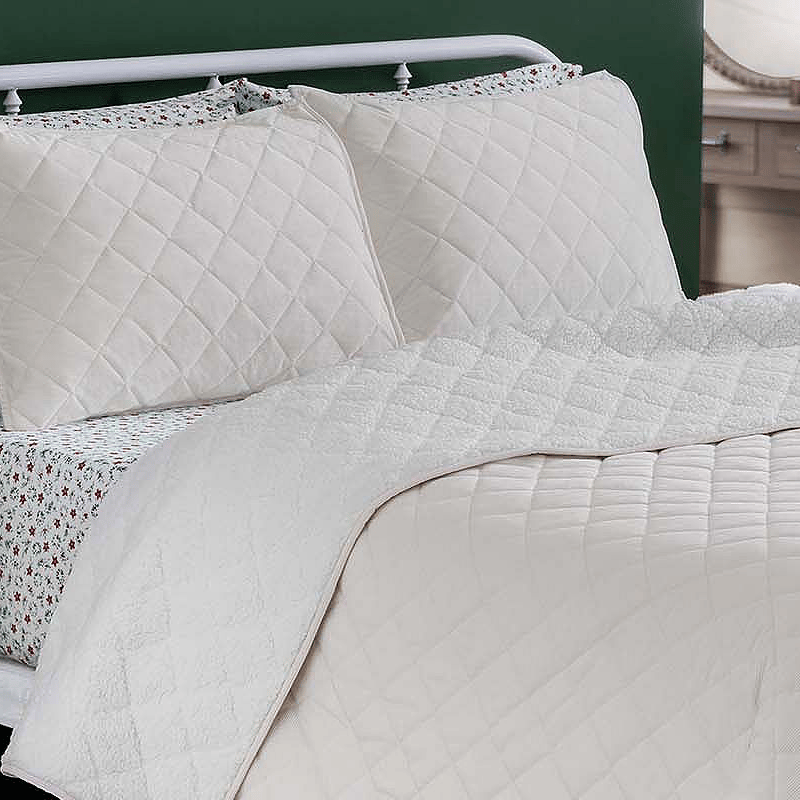 Martha Stewart Queen Sherpa Quilt Set features a quilted white design with matching pillow shams and patterned sheets underneath, creating a cozy and elegant look.