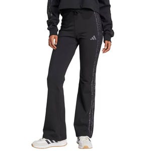 Black Adidas flare pants with a small logo on the thigh and patterned stripes down the sides, paired with white sneakers with black stripes.