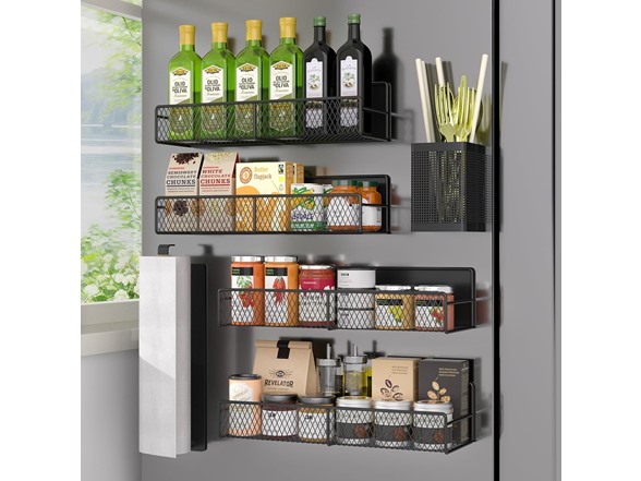 Wall-mounted metal racks hold bottles of olive oil, packaged snacks, canned goods, and jars. A utensil holder contains kitchen tools, and there is a paper towel dispenser on the side. The setup maximizes kitchen storage efficiently.