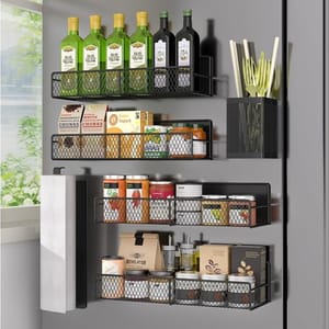 Wall-mounted metal racks hold bottles of olive oil, packaged snacks, canned goods, and jars. A utensil holder contains kitchen tools, and there is a paper towel dispenser on the side. The setup maximizes kitchen storage efficiently.