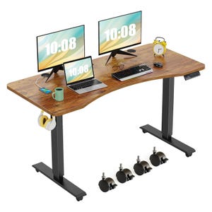 An electric standing desk with a wood grain surface, featuring two monitors, a laptop, a smartphone, a mug, and a keyboard. It includes a yellow clock, headphones on a hook, and comes with four caster wheels for mobility.