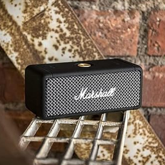 A black Marshall portable speaker on a metal grate with a brick wall in the background.
