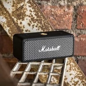 A black Marshall portable speaker on a metal grate with a brick wall in the background.