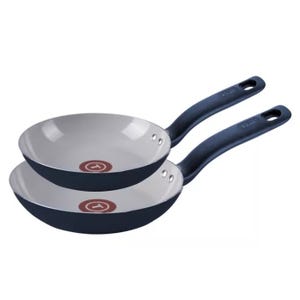 Two T-Fal nonstick frying pans with blue exteriors and white interiors are shown. Each has a comfortable handle with a hole for hanging.
