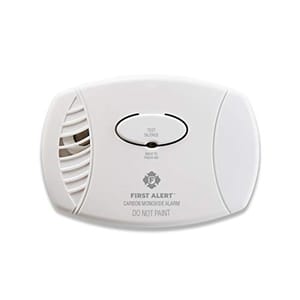 White, oval-shaped carbon monoxide detector with a test/silence button in the center and vents on the left side, labeled 'First Alert.'