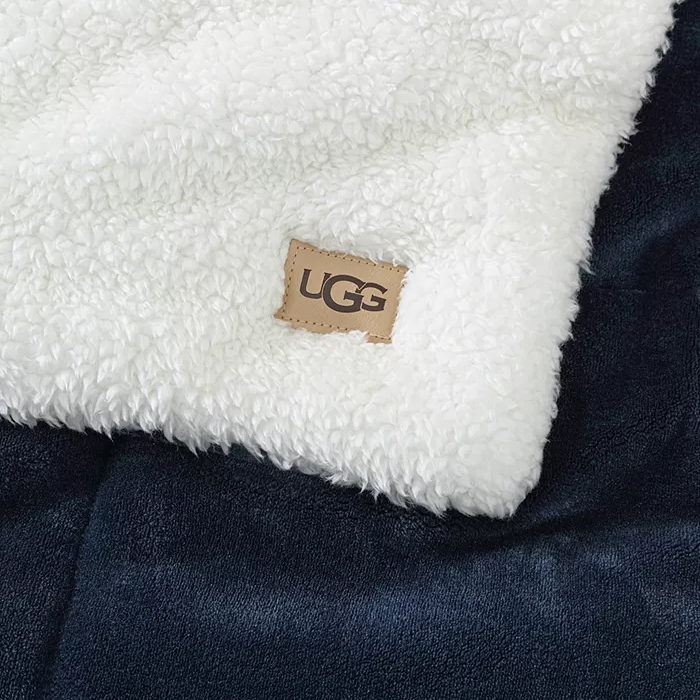 UGG label on a white, fluffy textile with a dark blue background, suggesting a piece of clothing or accessory.