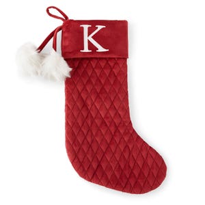 Red quilted Christmas stocking with a white letter 'K' on the cuff and white pom-poms.