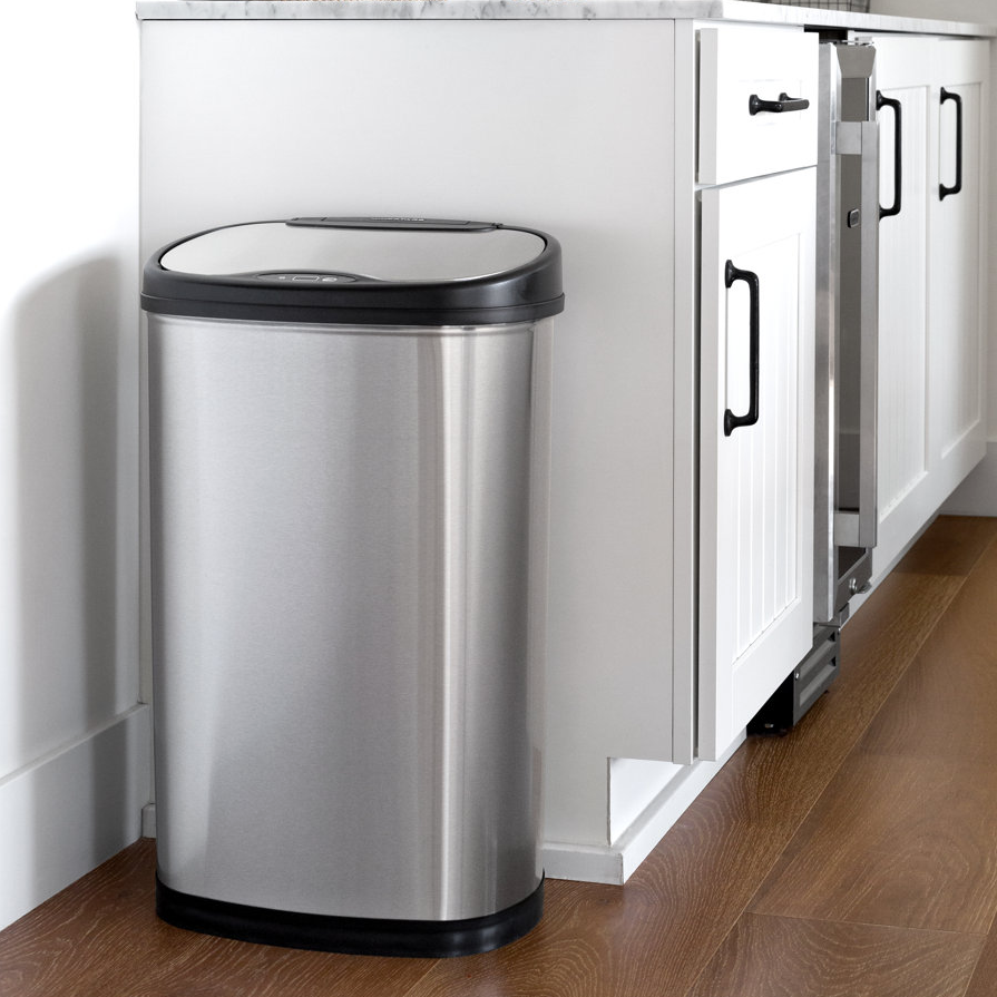 A stainless steel trash can with a black lid, placed beside white kitchen cabinets.