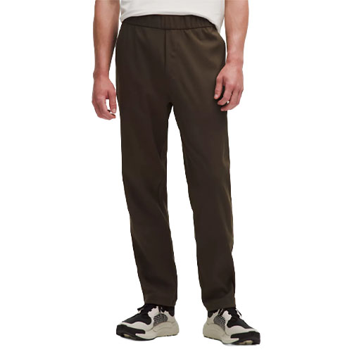 A person wearing dark brown pants with an elastic waistband, paired with white and black sneakers, and a white shirt.