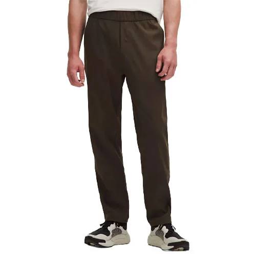 A person wearing dark brown pants with an elastic waistband, paired with white and black sneakers, and a white shirt.