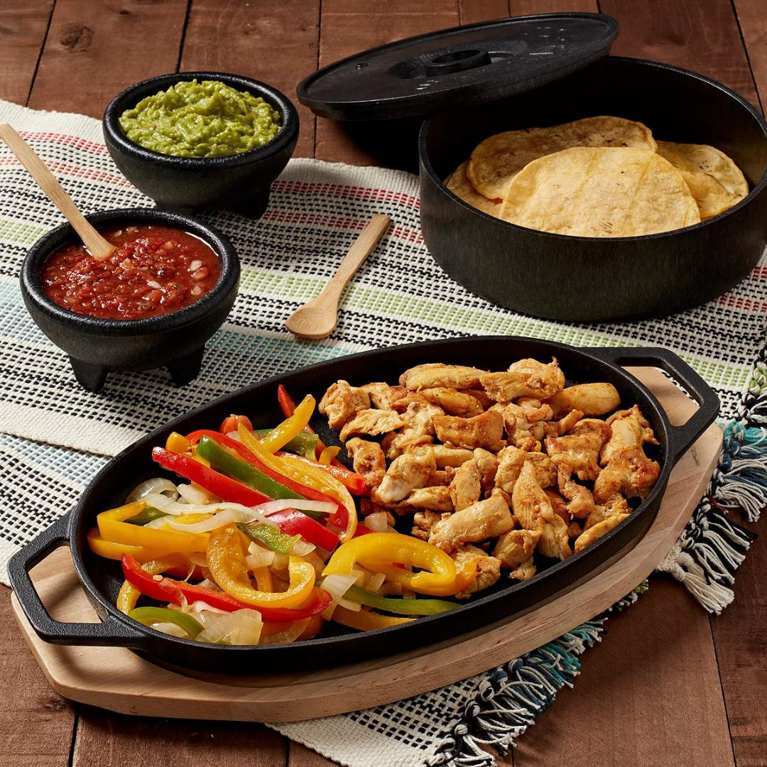 A sizzling fajita platter with chicken, onions, and bell peppers; accompanied by sides of guacamole, salsa, and tortillas.