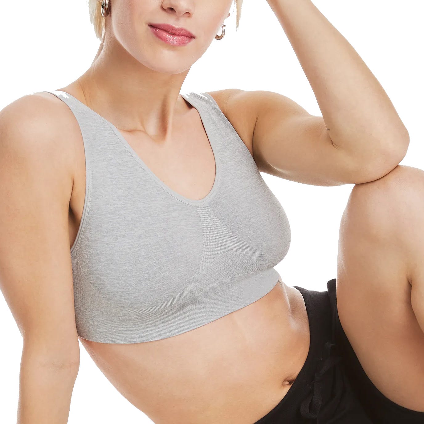 A person is wearing a light gray sports bra and black pants, sitting with one arm resting on their knee.