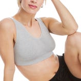 A person is wearing a light gray sports bra and black pants, sitting with one arm resting on their knee.