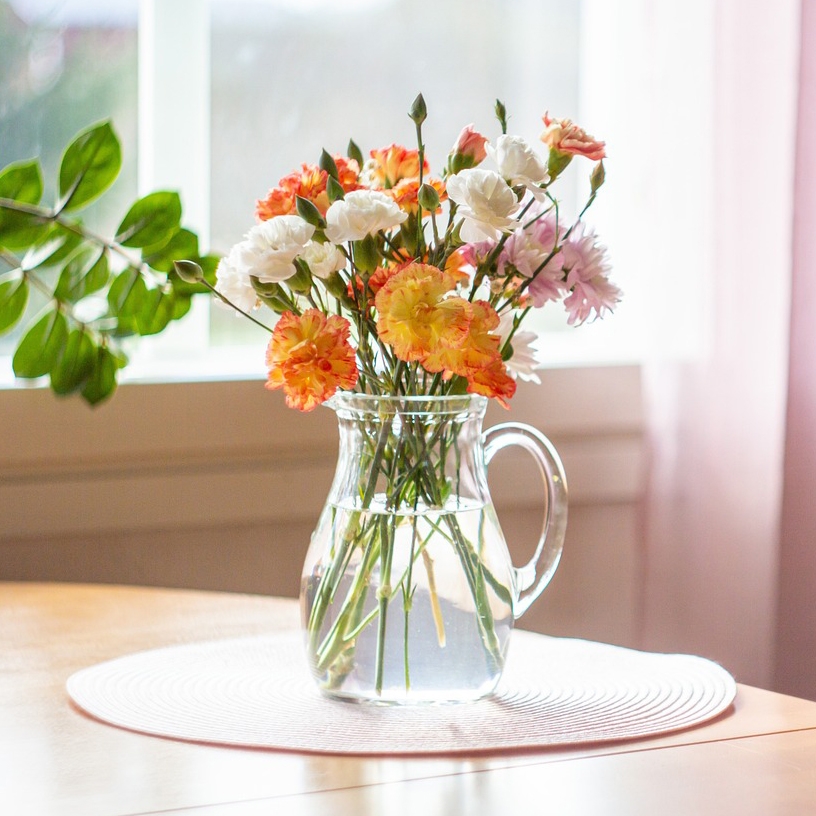 A clear glass pitcher filled with multicolored flowers on a white placemat.