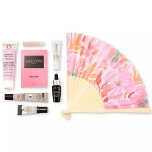 A collection of beauty products including body scrub, perfume sample, lip balm, moisturizer, serum, and sunscreen, accompanied by a decorative folding fan with a pink floral design.