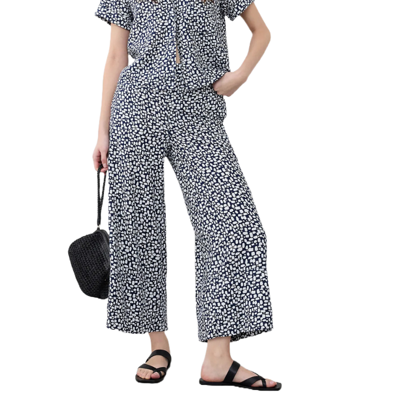 A person is wearing a short-sleeved, black and white patterned blouse paired with matching wide-leg pants. They are carrying a black woven handbag and wearing black sandals.