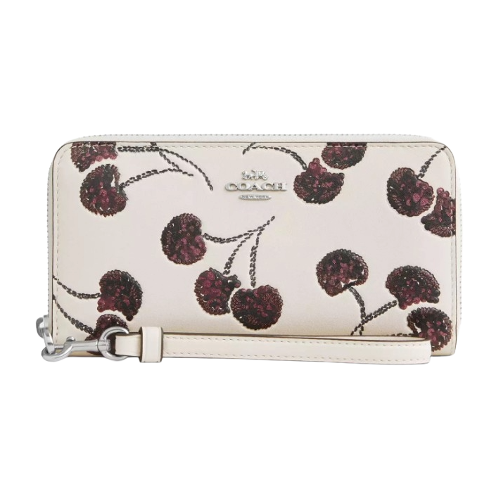 A wristlet featuring a light background with a pattern of dark red cherries and a Coach logo in the center.
