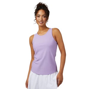 A woman is wearing a sleeveless lavender tank top with white pants, standing and smiling against a white background.