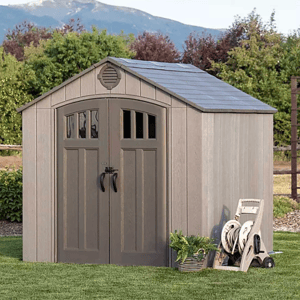 Suncast 8' Storage Shed features a double-door design with arched windows, shingle-style roof, and neutral color. A garden hose reel and potted plant are placed nearby, highlighting its use in a backyard setting.