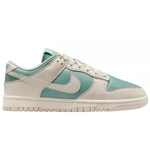 A pair of low-top sneakers in seafoam green and white with a prominent swoosh symbol on the side, featuring a white sole and perforations on the toe box.